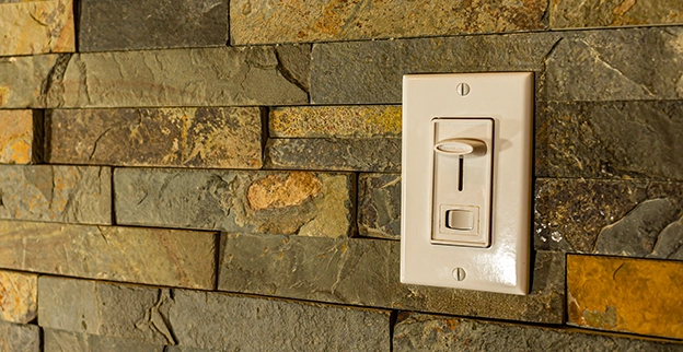 A white light switch mounted on a textured stone wall.