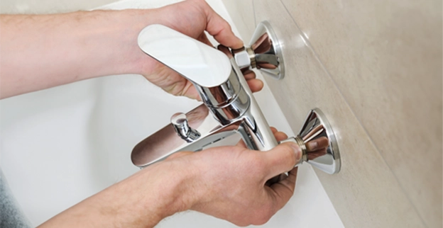 A person installs a sleek chrome faucet in a modern bathroom, adjusting its handles against a tiled wall.