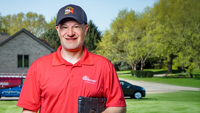 A handyman in a red polo shirt and cap stands outdoors.