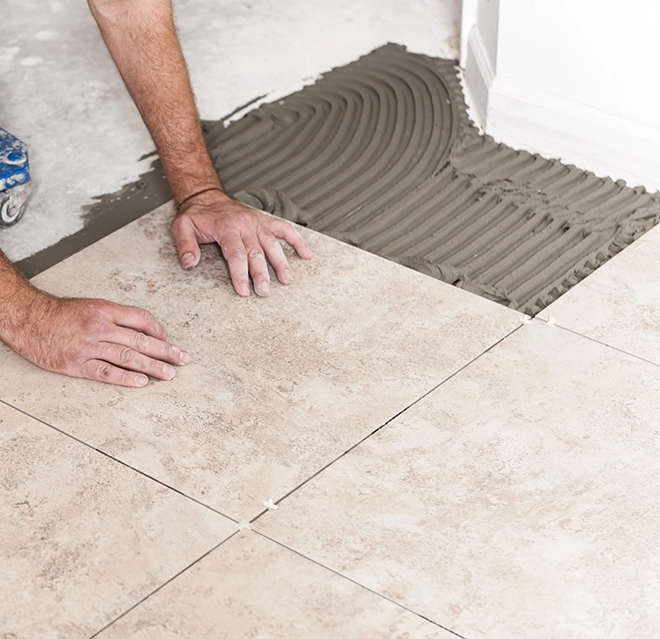 A worker places tile on a floor using hands to adjust its position.
