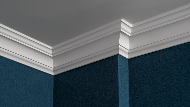 Close-up of a ceiling corner featuring elegant white crown molding meeting a textured dark teal wall.