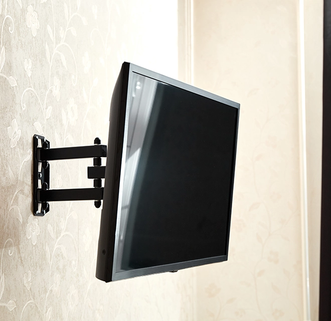 A sleek, black wall-mounted TV is positioned at an angle against a subtle floral wallpaper background.