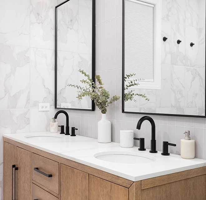 Modern bathroom featuring two sinks, dark fixtures, a wooden vanity and greenery in a vase.