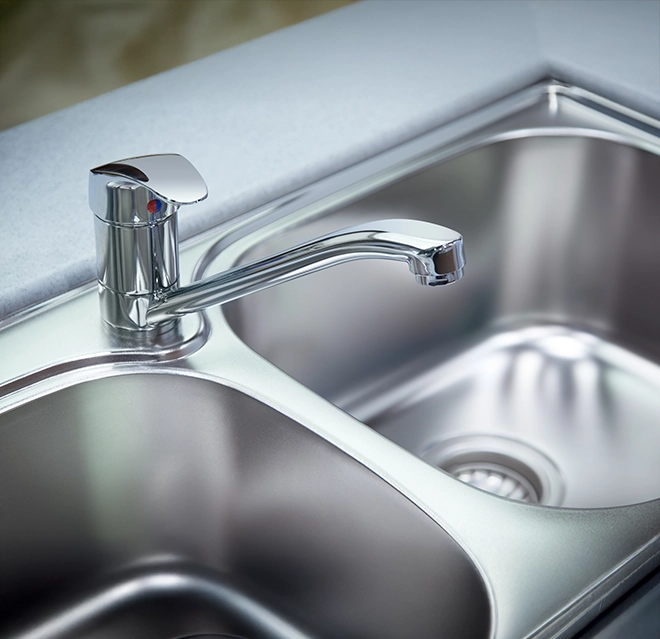 A modern chrome kitchen faucet beside a stainless steel sink with a smooth countertop.