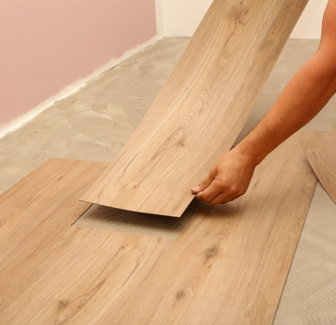 A close-up of a hand laying wooden flooring planks on a light-colored surface.