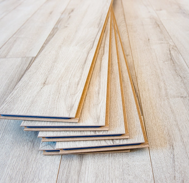 Stack of light-colored laminate flooring planks arranged on a wooden surface.