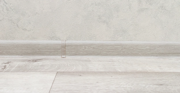 Close-up of light-colored laminate flooring meeting a textured wall.