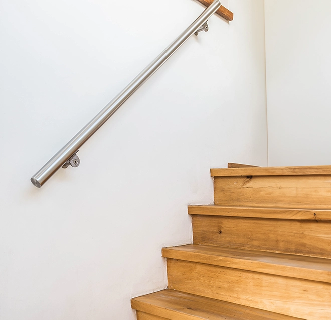 Wooden staircase with a silver handrail against a clean white wall.