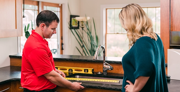 A man measures a countertop with a tape measure in a kitchen setting.