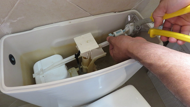 A person using pliers to repair the internal mechanism of a toilet tank.