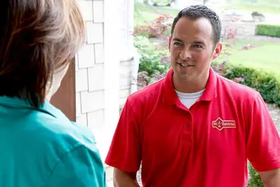 A Mr. Handyman carpenter greeting his customer at her front door