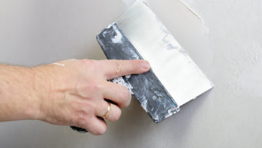 A handyman using a wide putty knife to apply and smooth out joint compound on a residential wall.