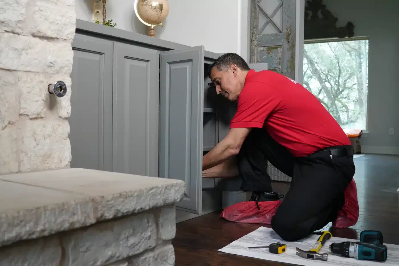 A Mr. Handyman service professional repairing cabinetry in a home.