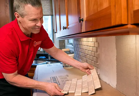 Handyman installing subway tile backsplash in kitchen.